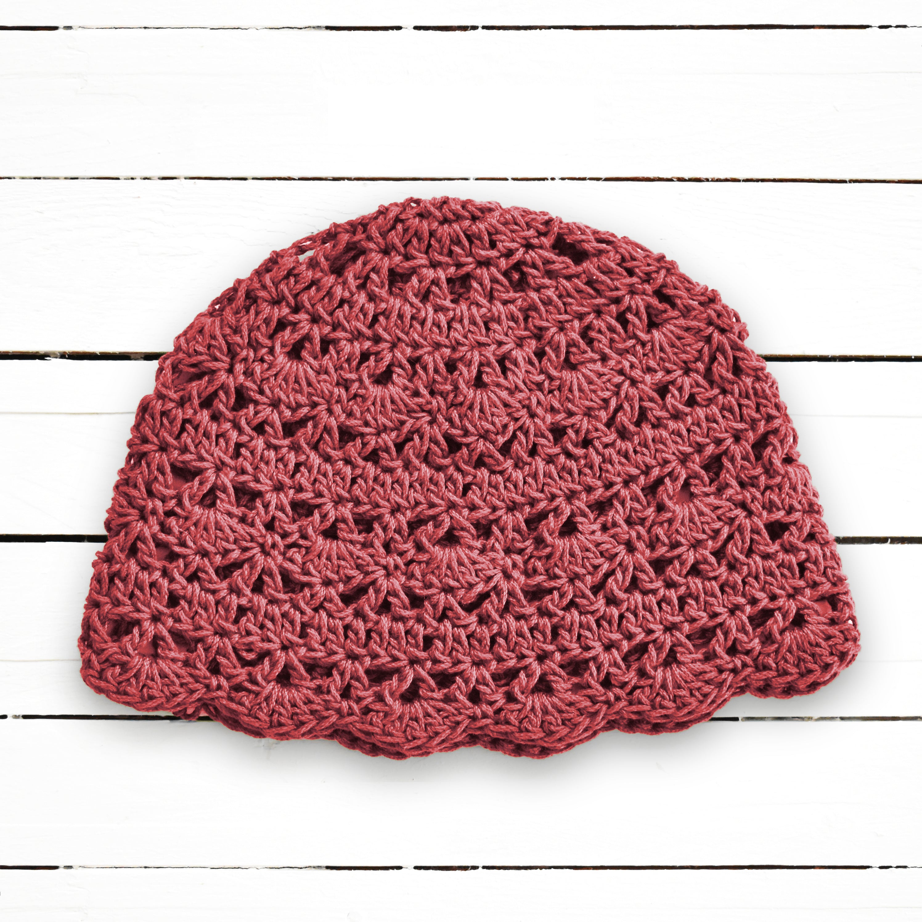 Terracotta pink lace crochet beanie on a white wooden background.