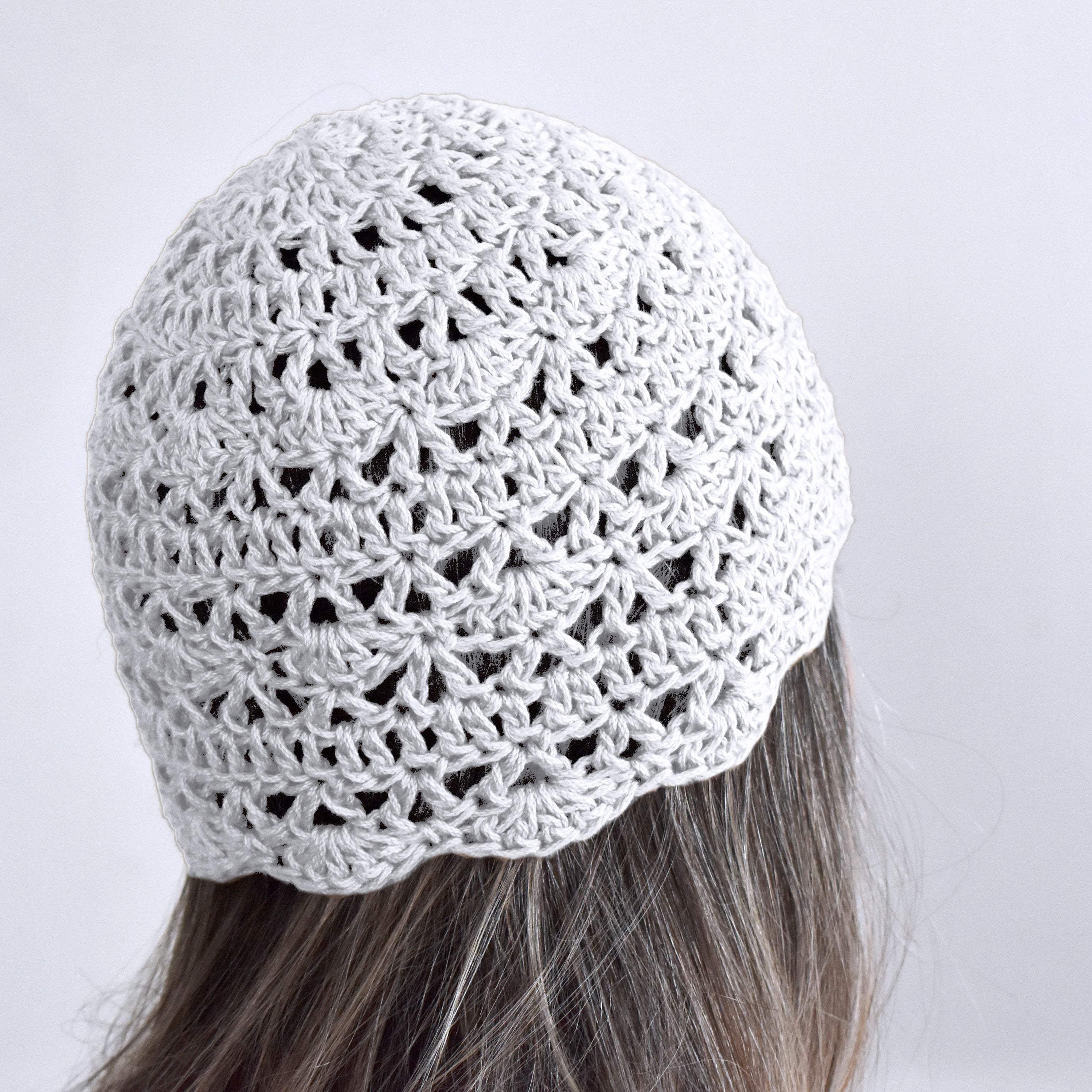 White crochet beanie worn by a person with gray hair on a white background.