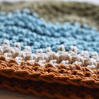 Close-up of a crocheted hat with green blue, white, and orange stripes.