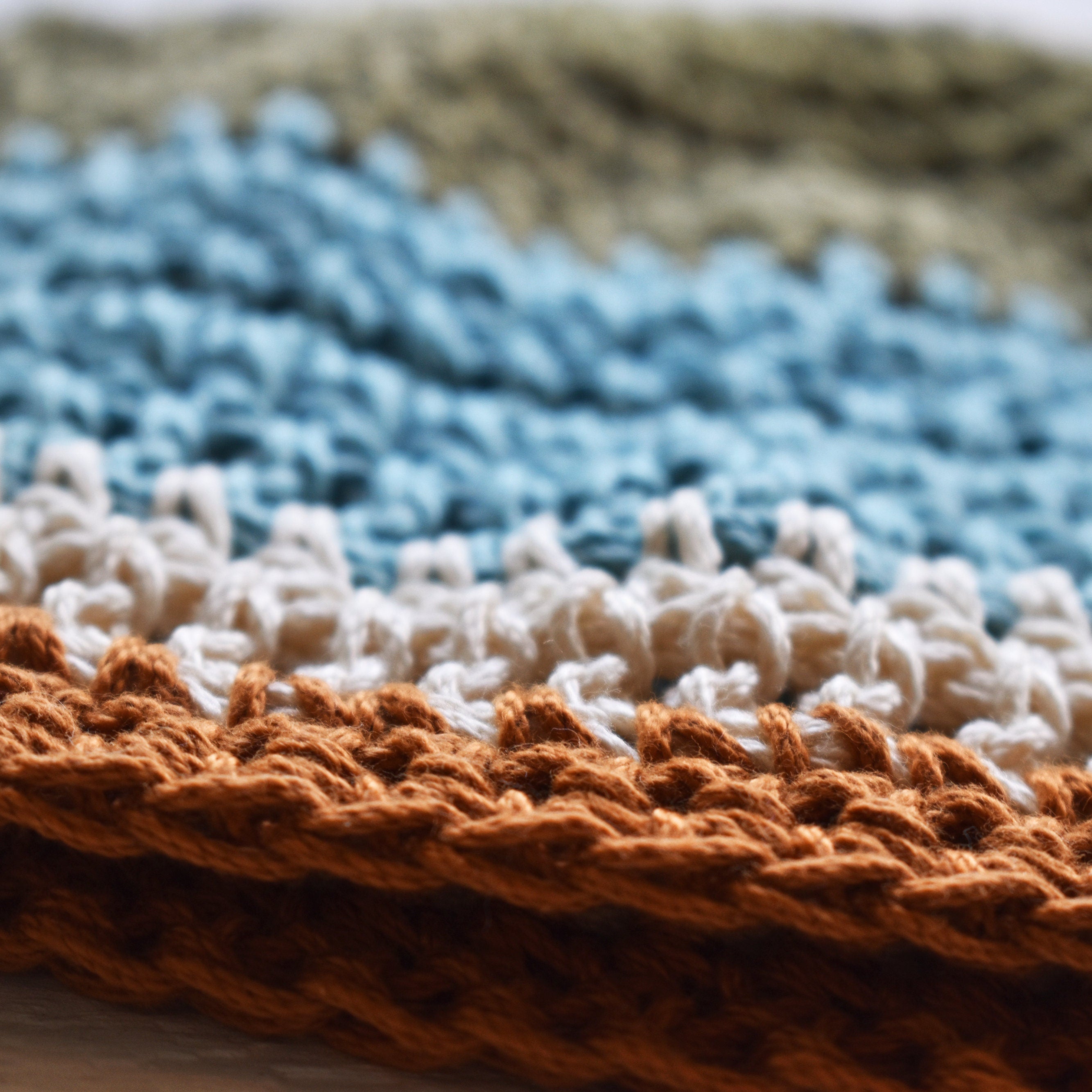 Close-up of a crocheted hat with green blue, white, and orange stripes.