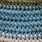 Close-up of crocheted hat with green, blue, and beige striped pattern.