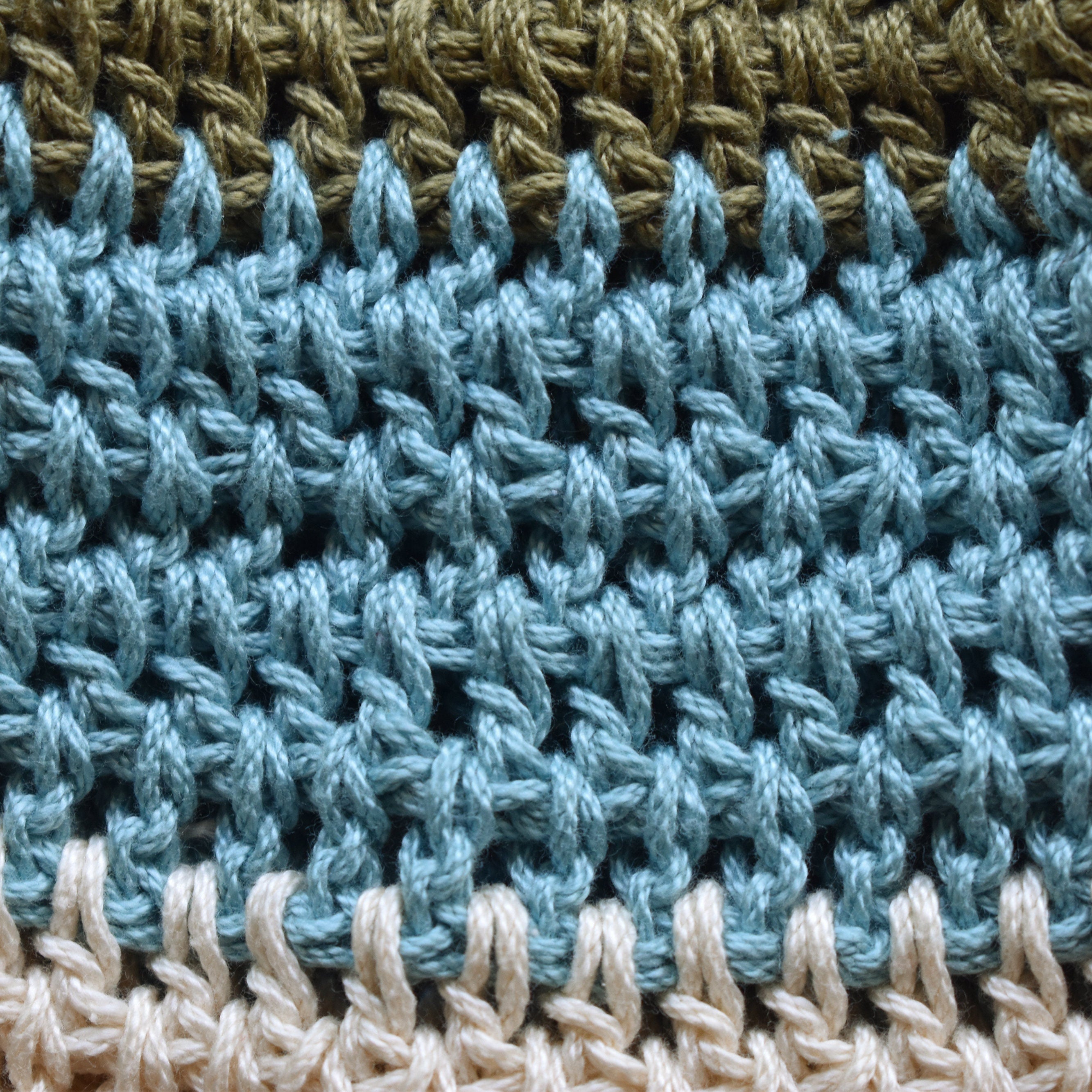 Close-up of crocheted hat with green, blue, and beige striped pattern.