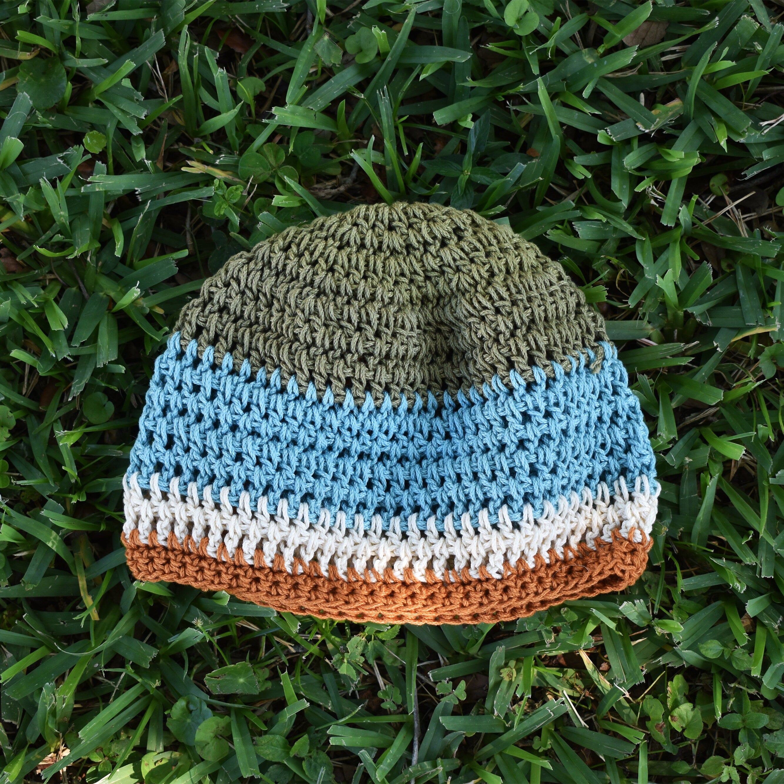 Crocheted beanie with striped colors on grass.