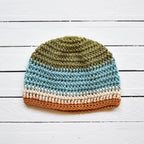 Crocheted beanie with green, light blue, beige, and orange striped colors on a white wooden surface.