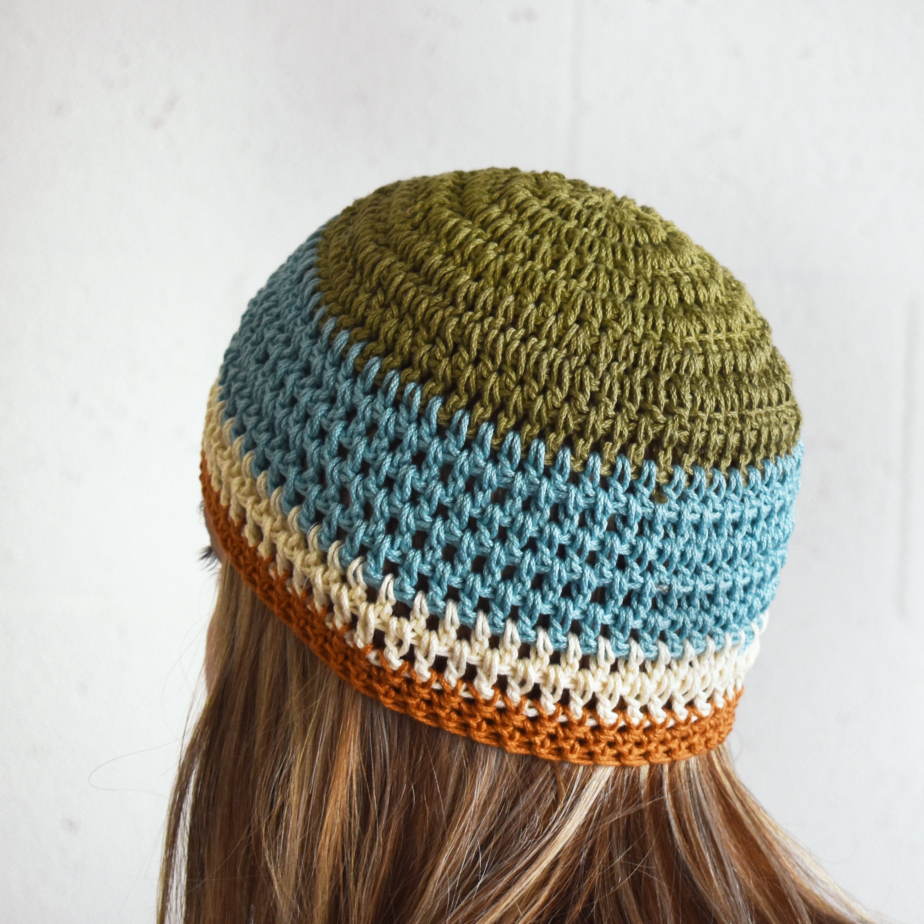 Colorful knitted beanie worn by a person with long hair against a plain background.