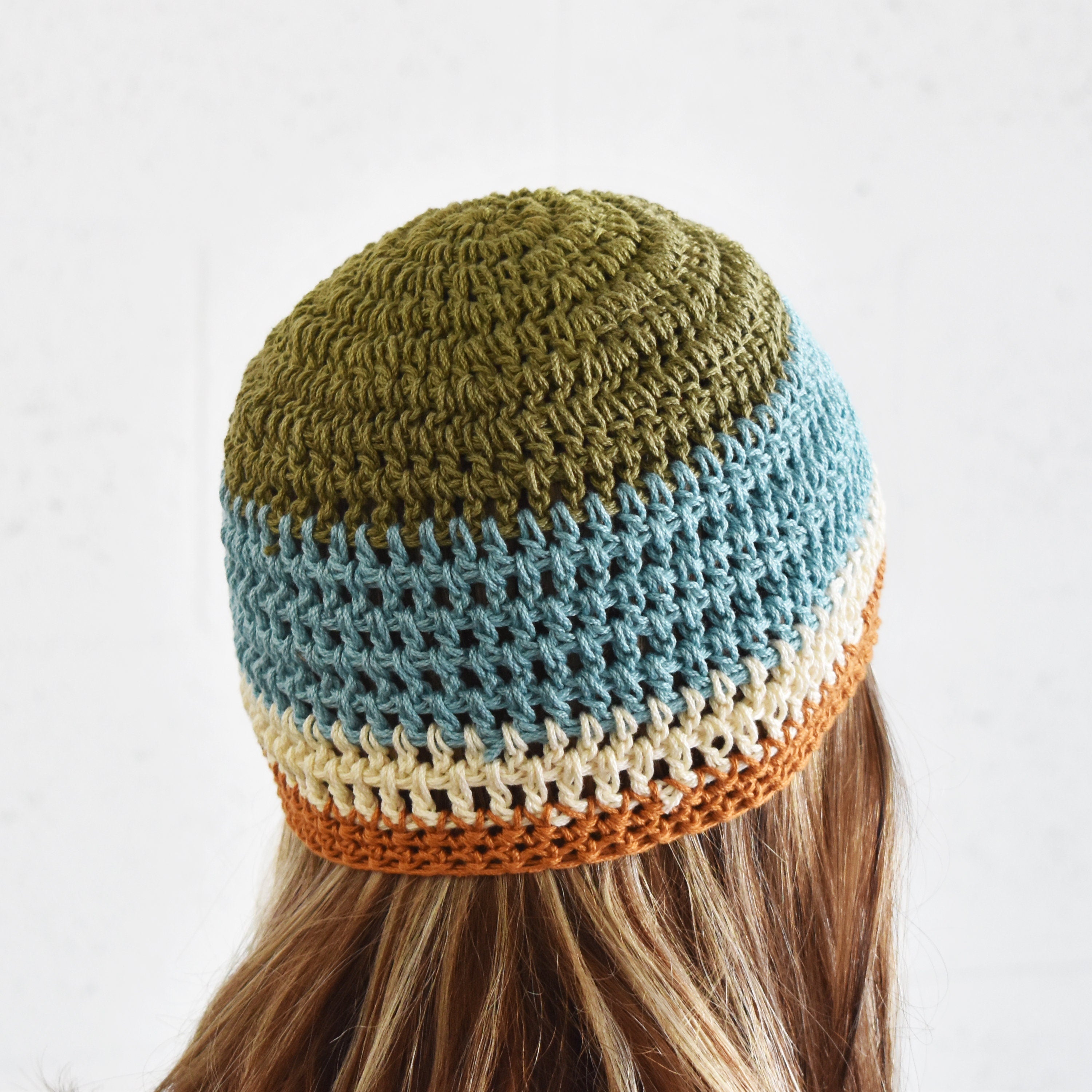 Person with long brown hair wearing a colorful knitted beanie with a striped pattern on a white background.