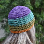 Colorful crocheted beanie worn by a person looking into a blurred green outdoor background.