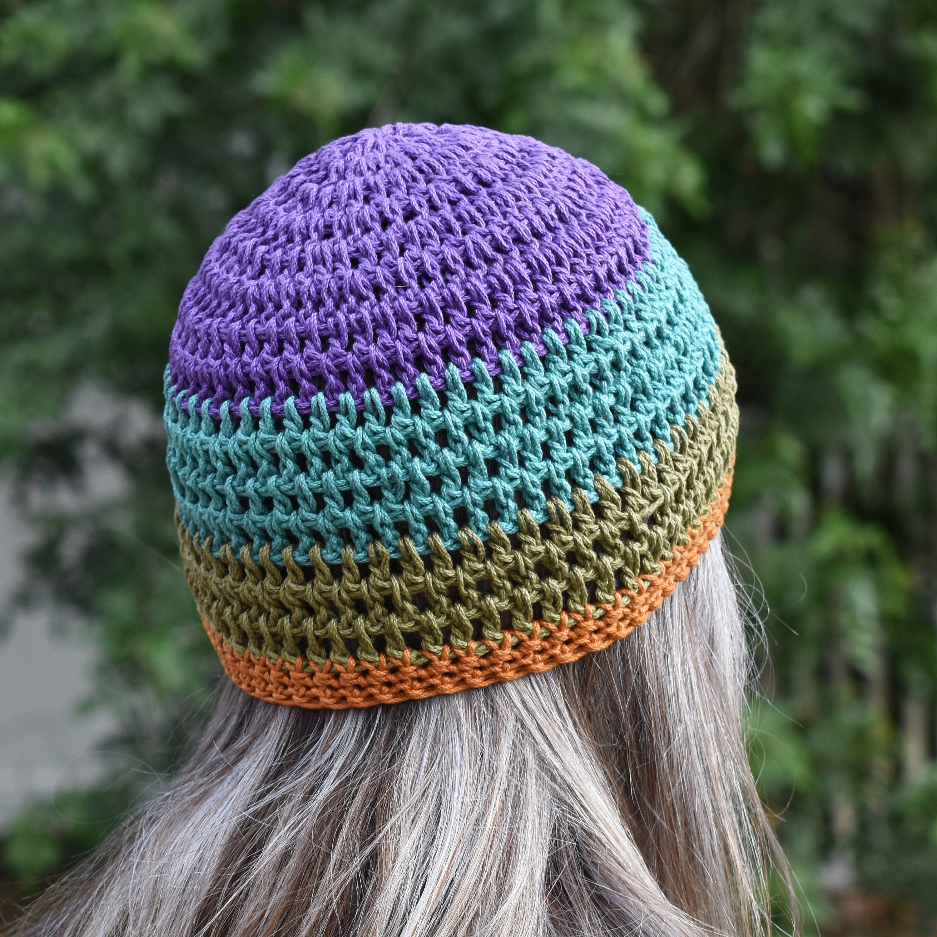 Colorful crocheted beanie worn by a person looking into a blurred green outdoor background.