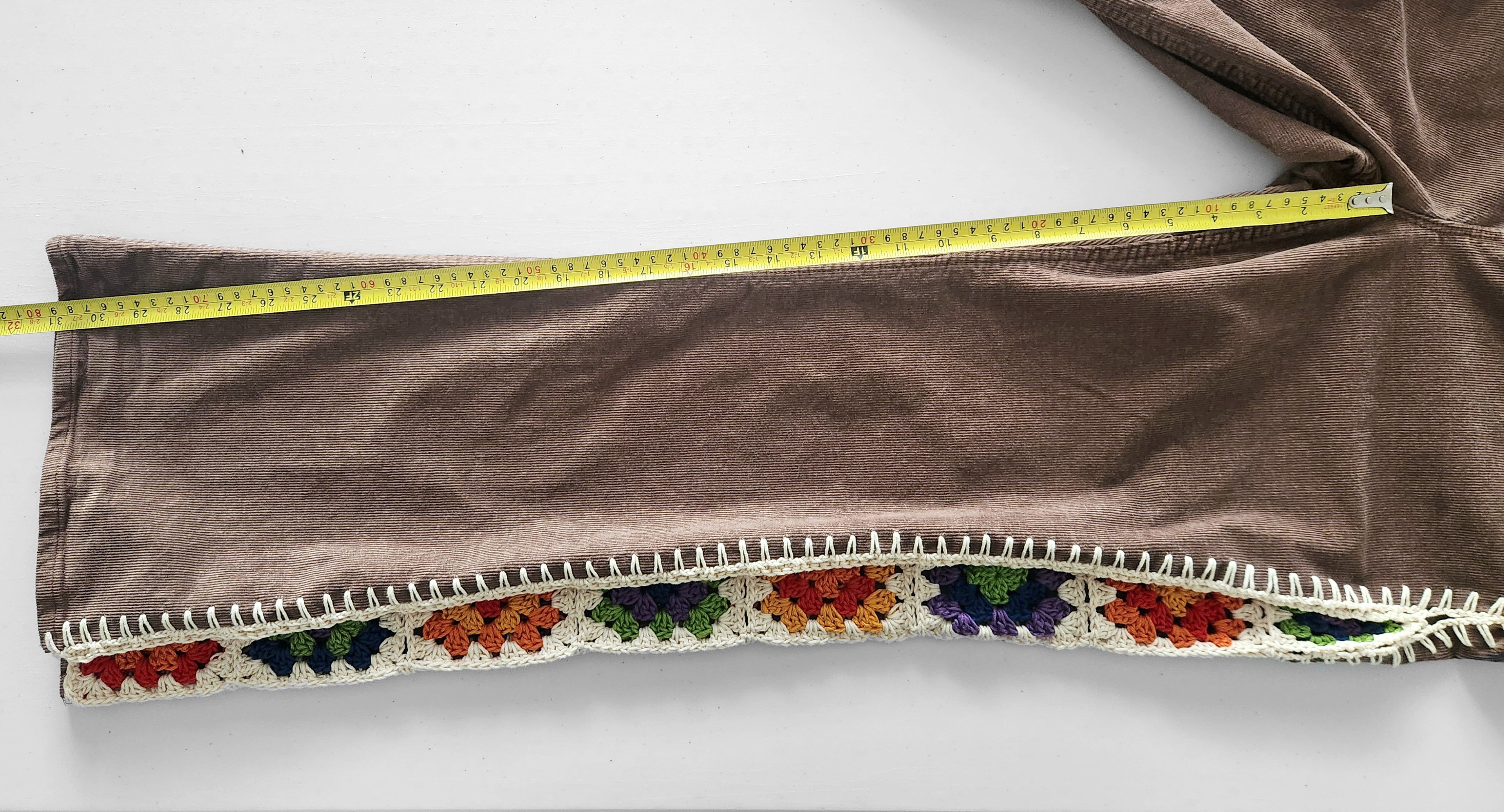 Measuring the inseam of brown corduroy pants with colorful crochet granny square inserts.