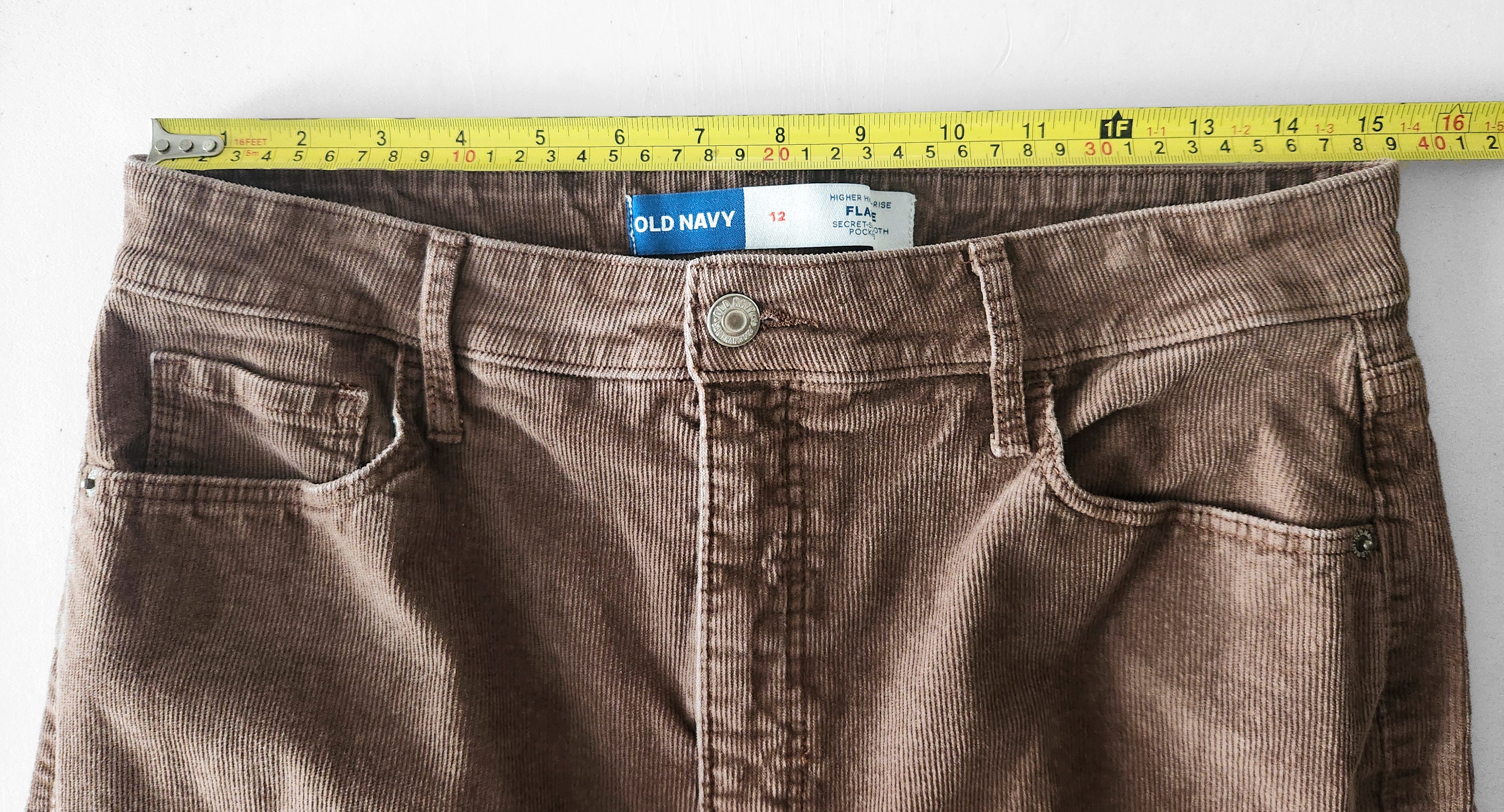 Brown corduroy pants with a measuring tape across the waist on a white background.