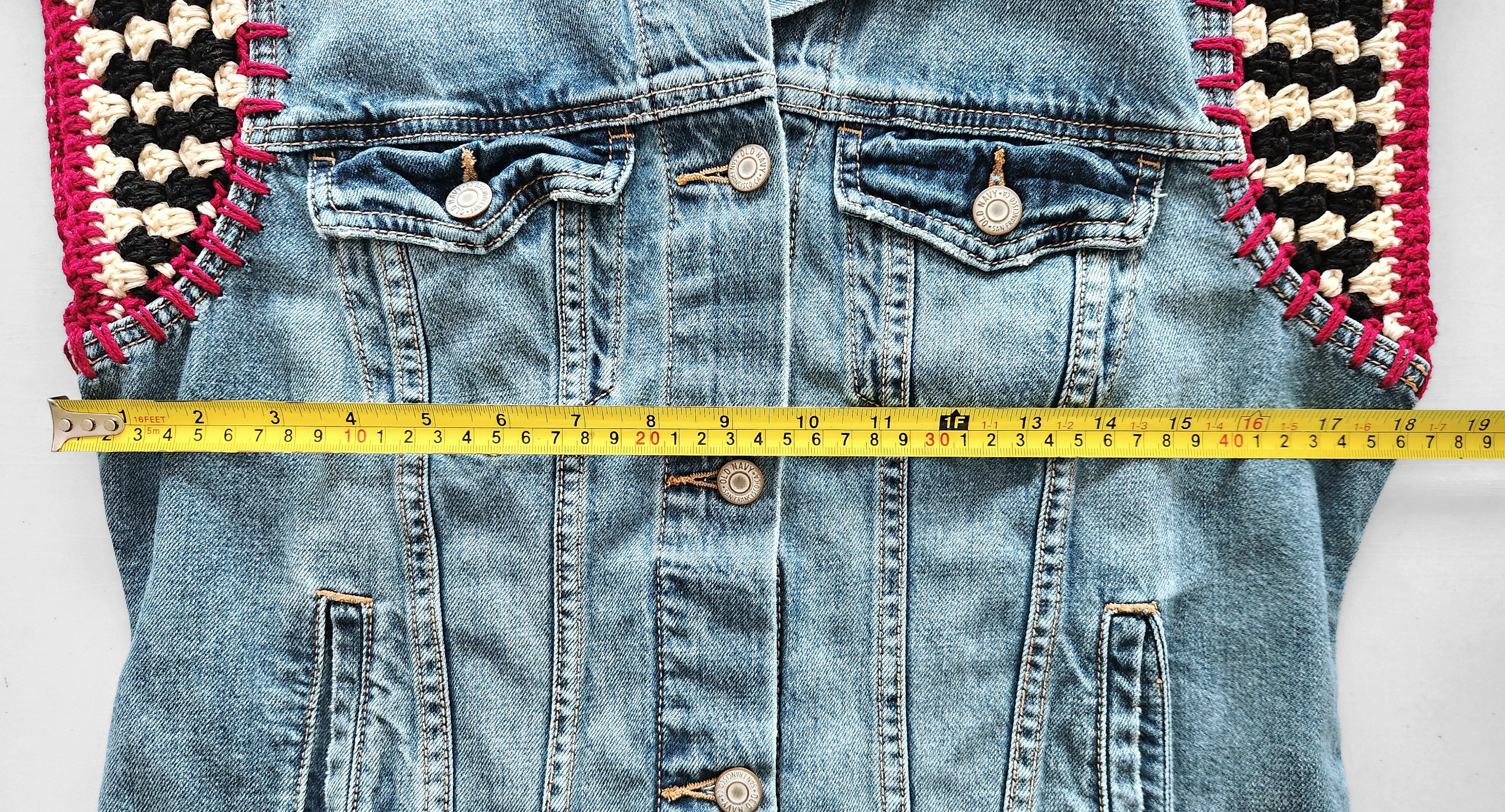 Blue denim jacket with decorative crochet cap sleeves and a measuring tape across the chest.