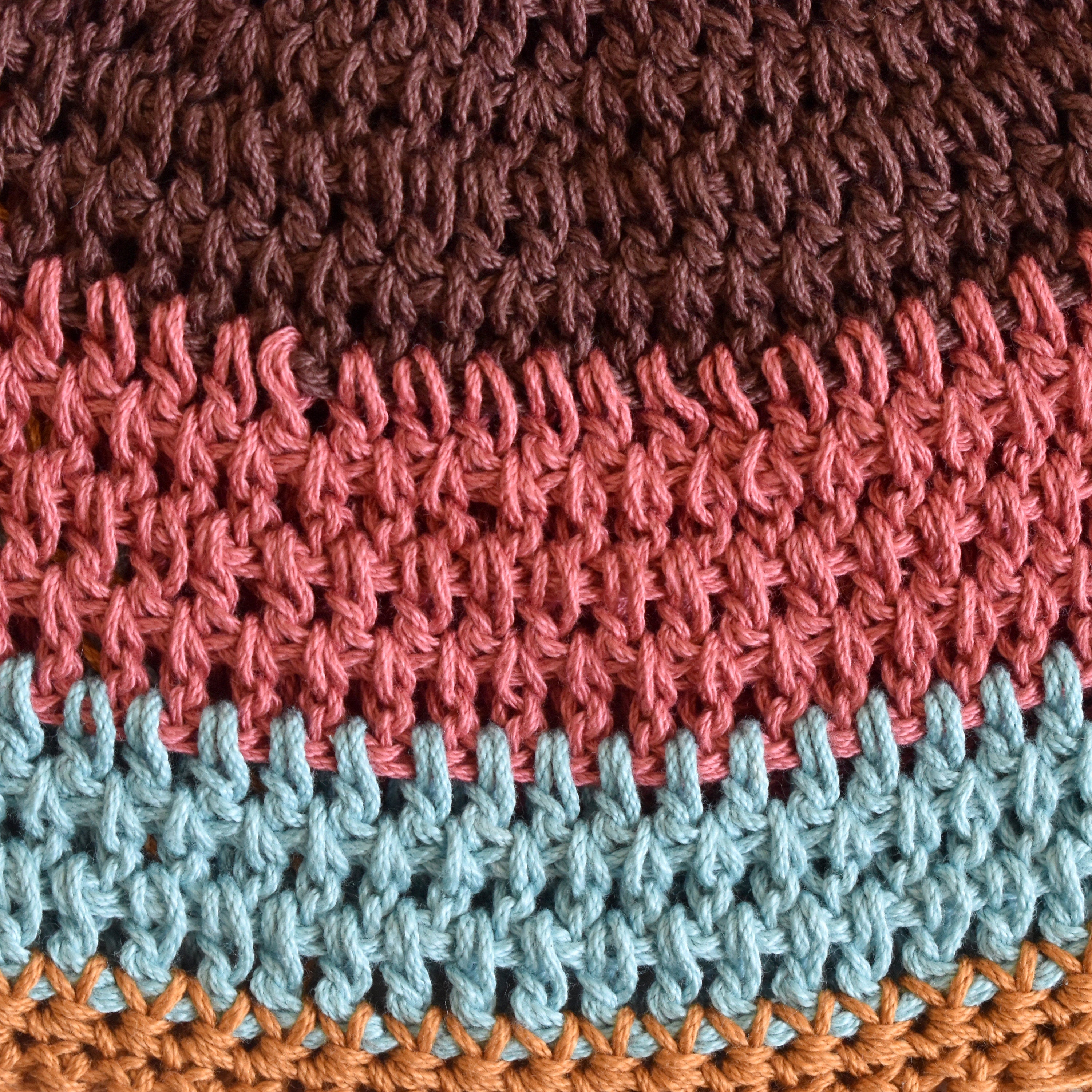 Close-up of a crocheted hat with a striped pattern in brown, pink, blue, and orange.