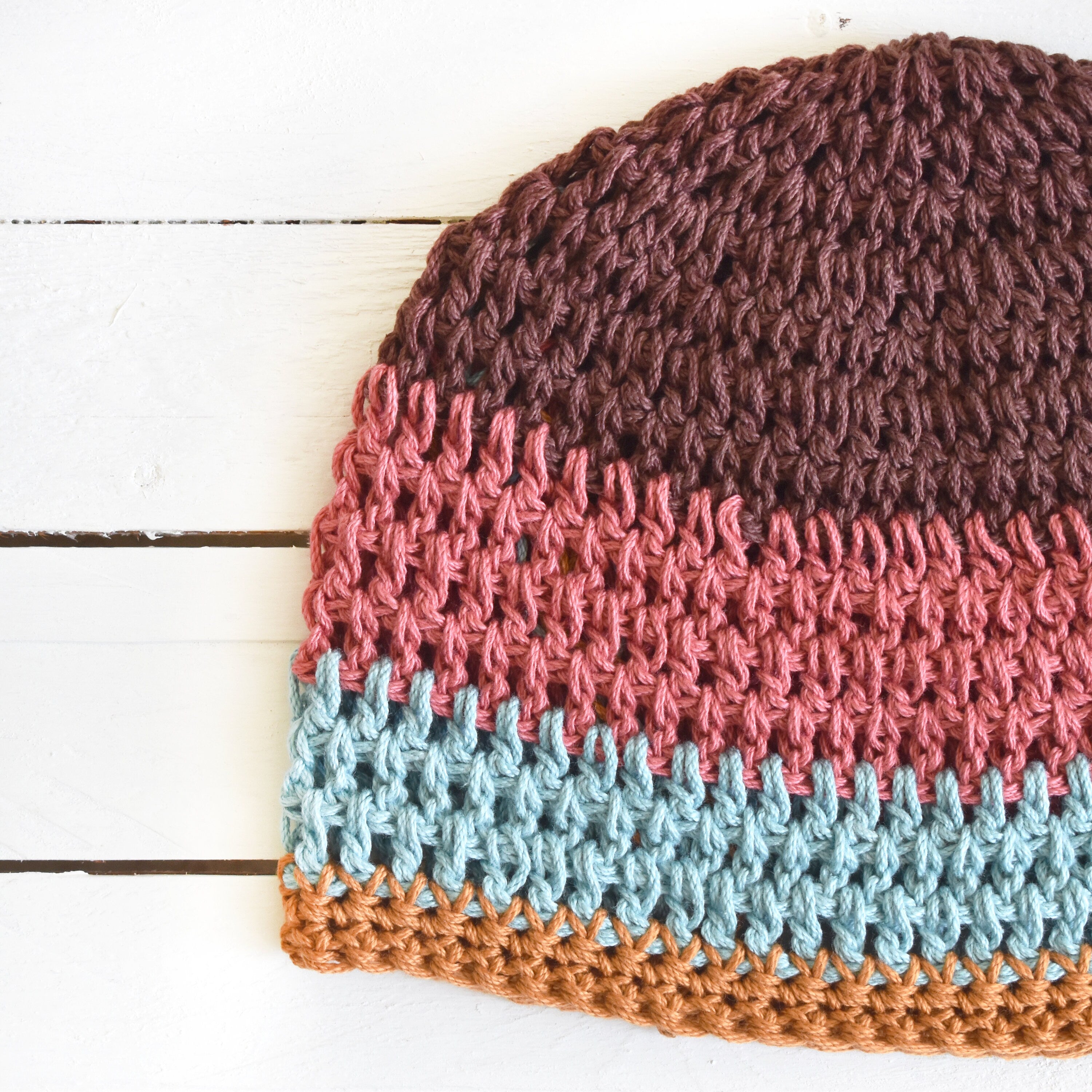 Multicolored crocheted beanie on a white wooden surface.