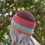 A person wearing a multicolored crocheted beanie in a blurred natural outdoor background.