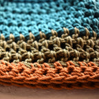 Close-up of crocheted hat in blue, green, and orange on a textured surface.