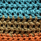 Close-up of crocheted hat with blue, green, and orange striped pattern.
