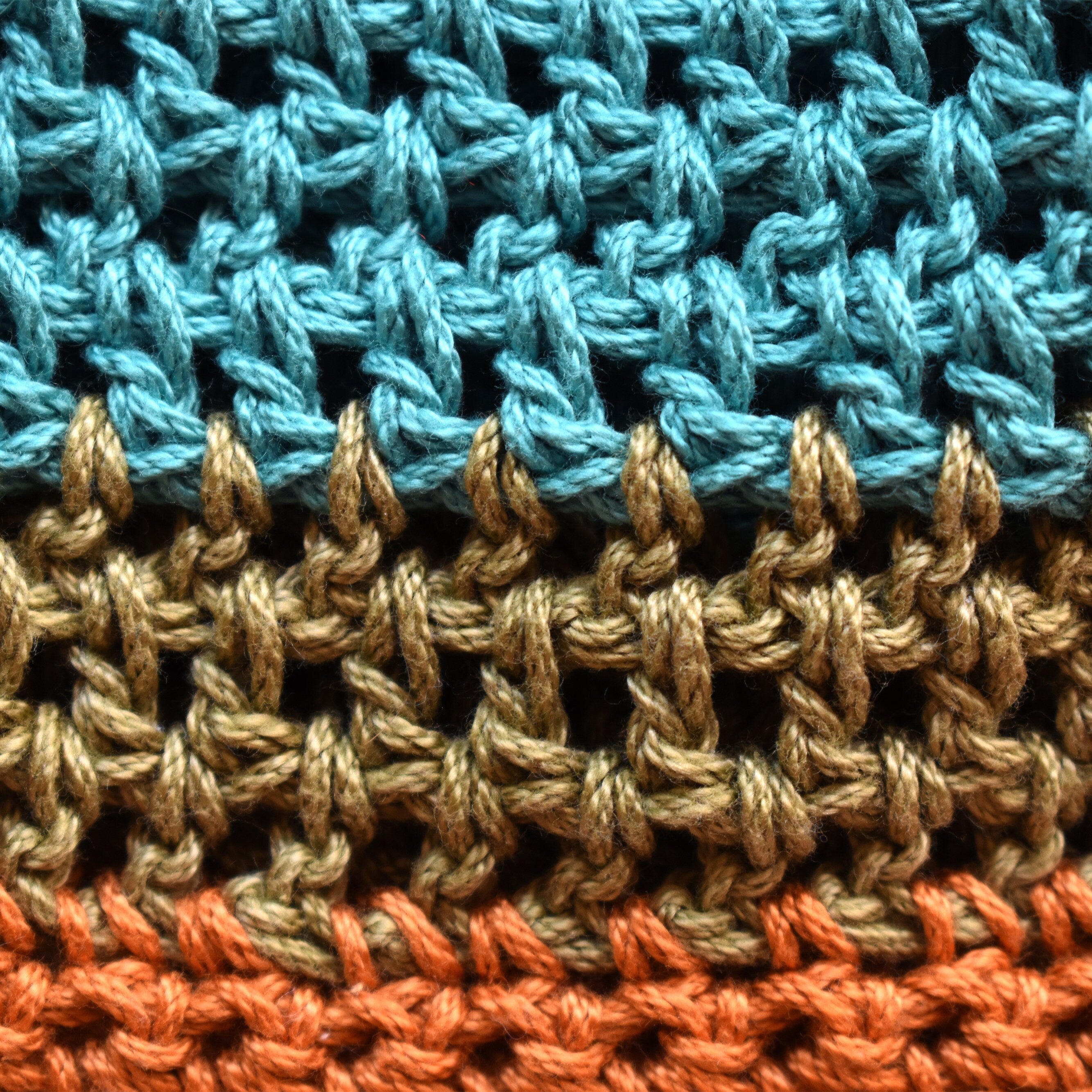 Close-up of crocheted hat with blue, green, and orange striped pattern.
