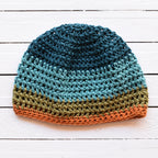Crocheted beanie with striped colors on a white wooden surface.