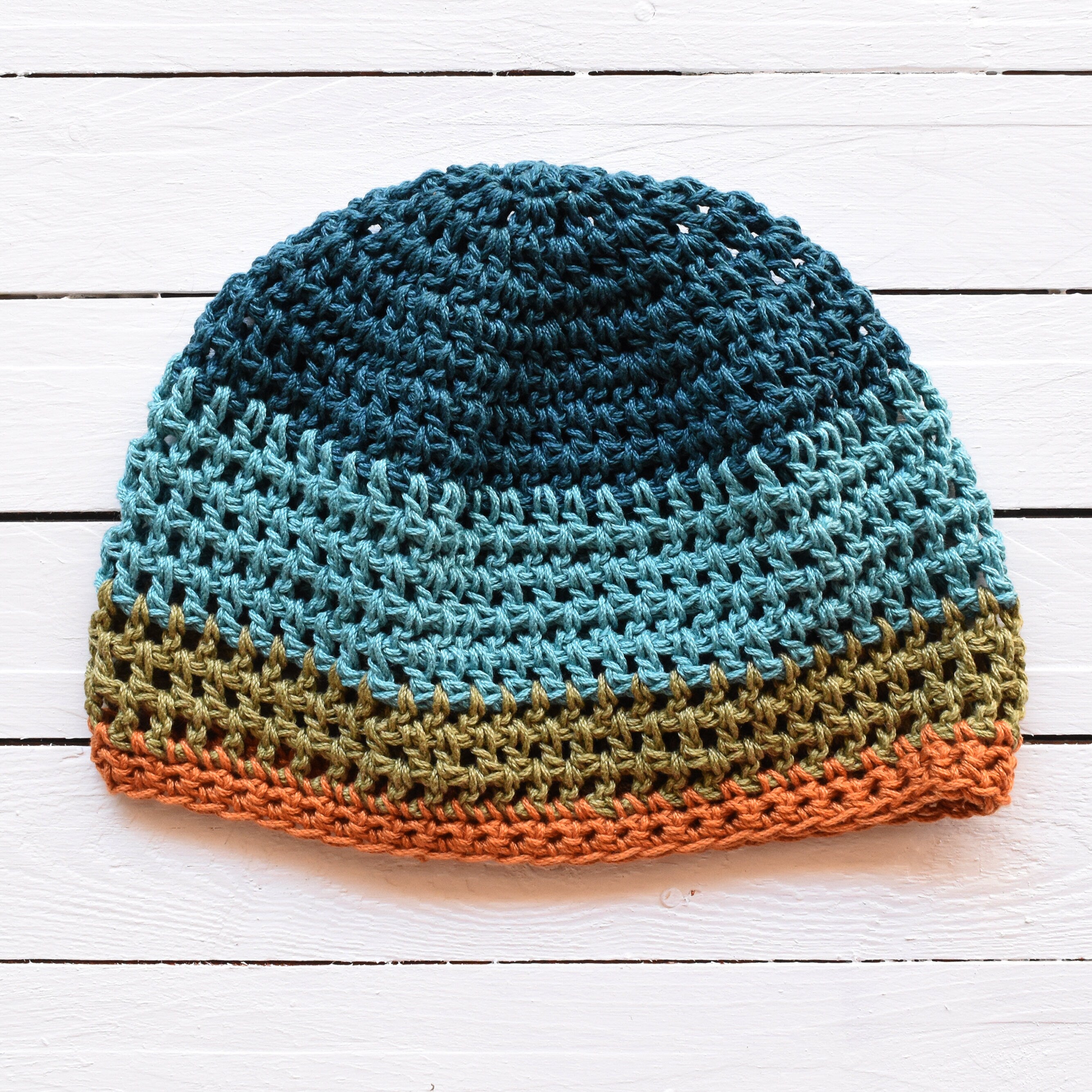 Crocheted beanie with striped colors on a white wooden surface.