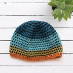 Crocheted beanie with striped colors on a white wooden surface.