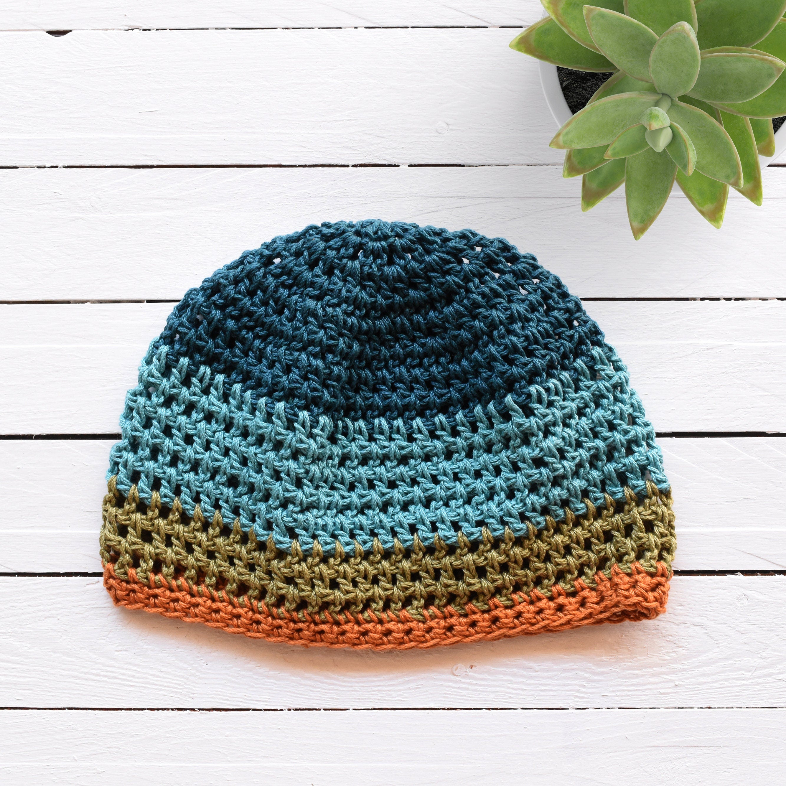 Crocheted beanie with striped colors on a white wooden surface.