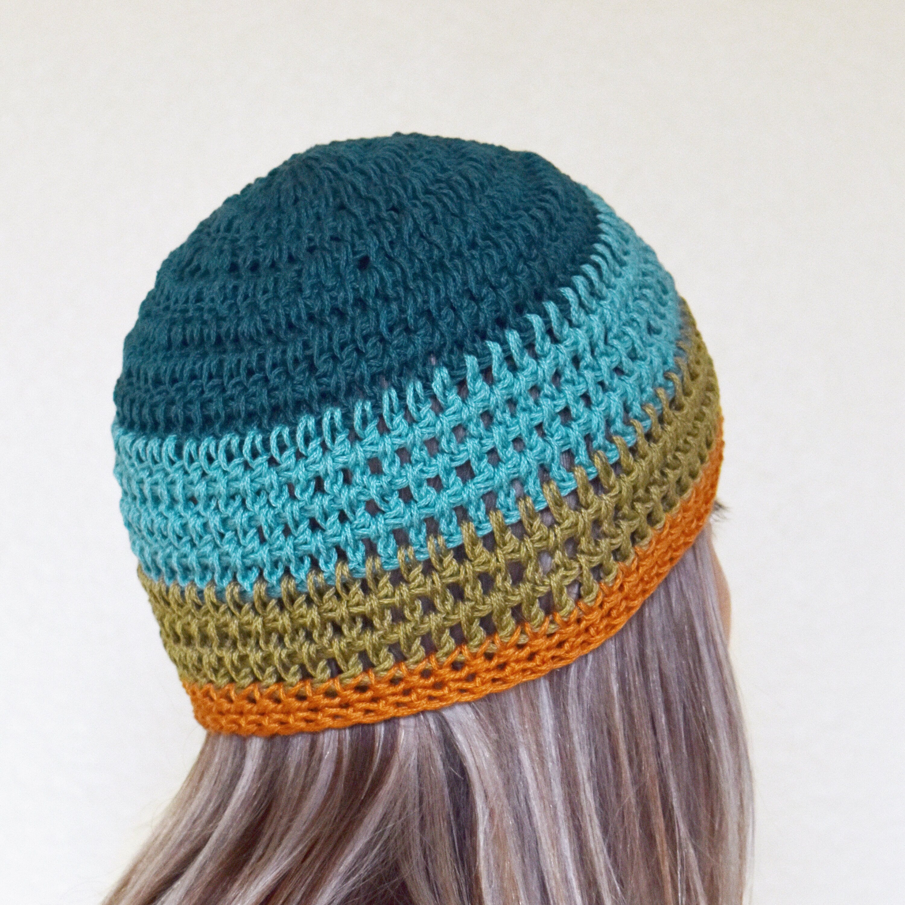 Colorful knitted beanie on a person with long hair against a neutral background.