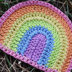 Colorful crocheted rainbow with pastel colors on grass.