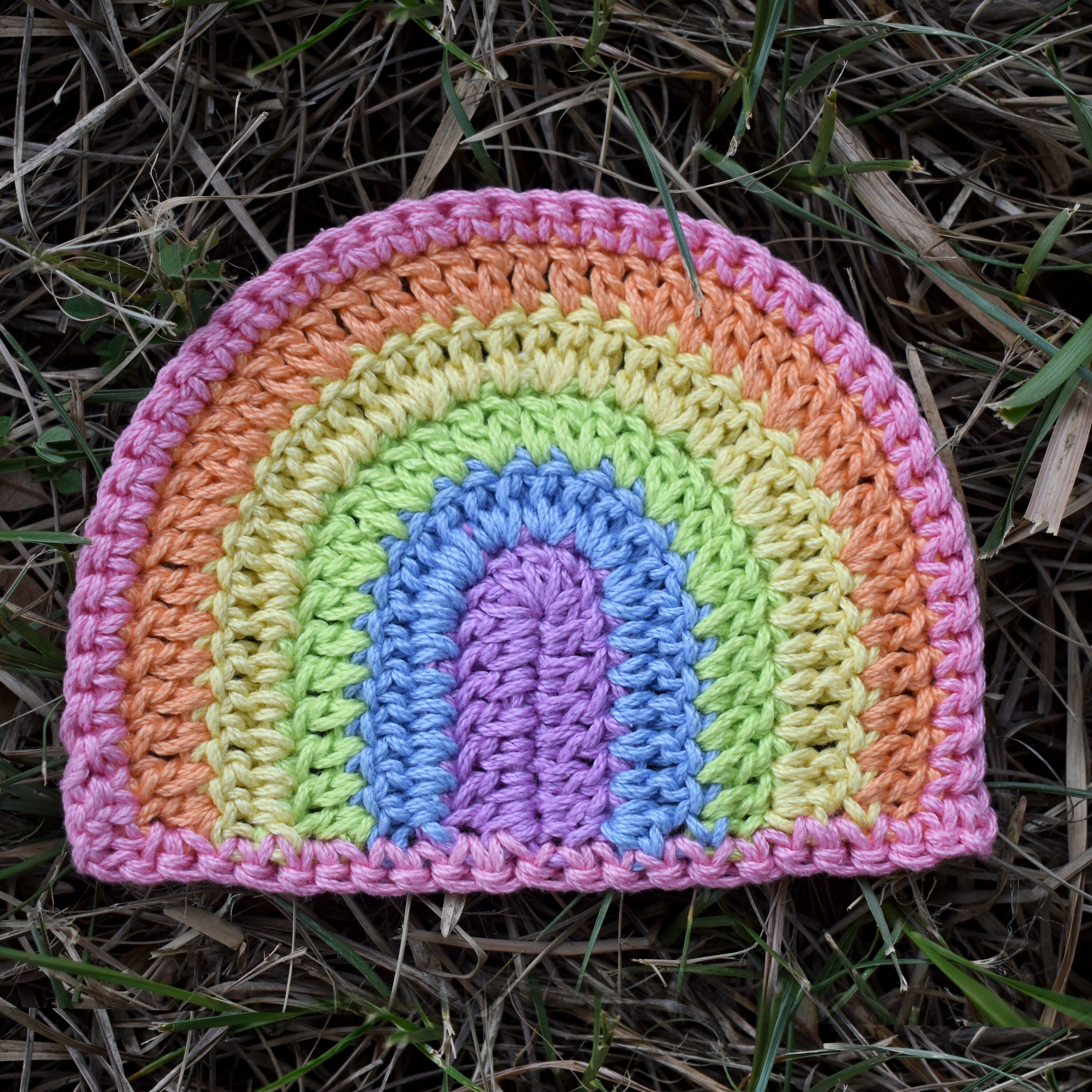 Crocheted rainbow patch with pastel colors on grass.