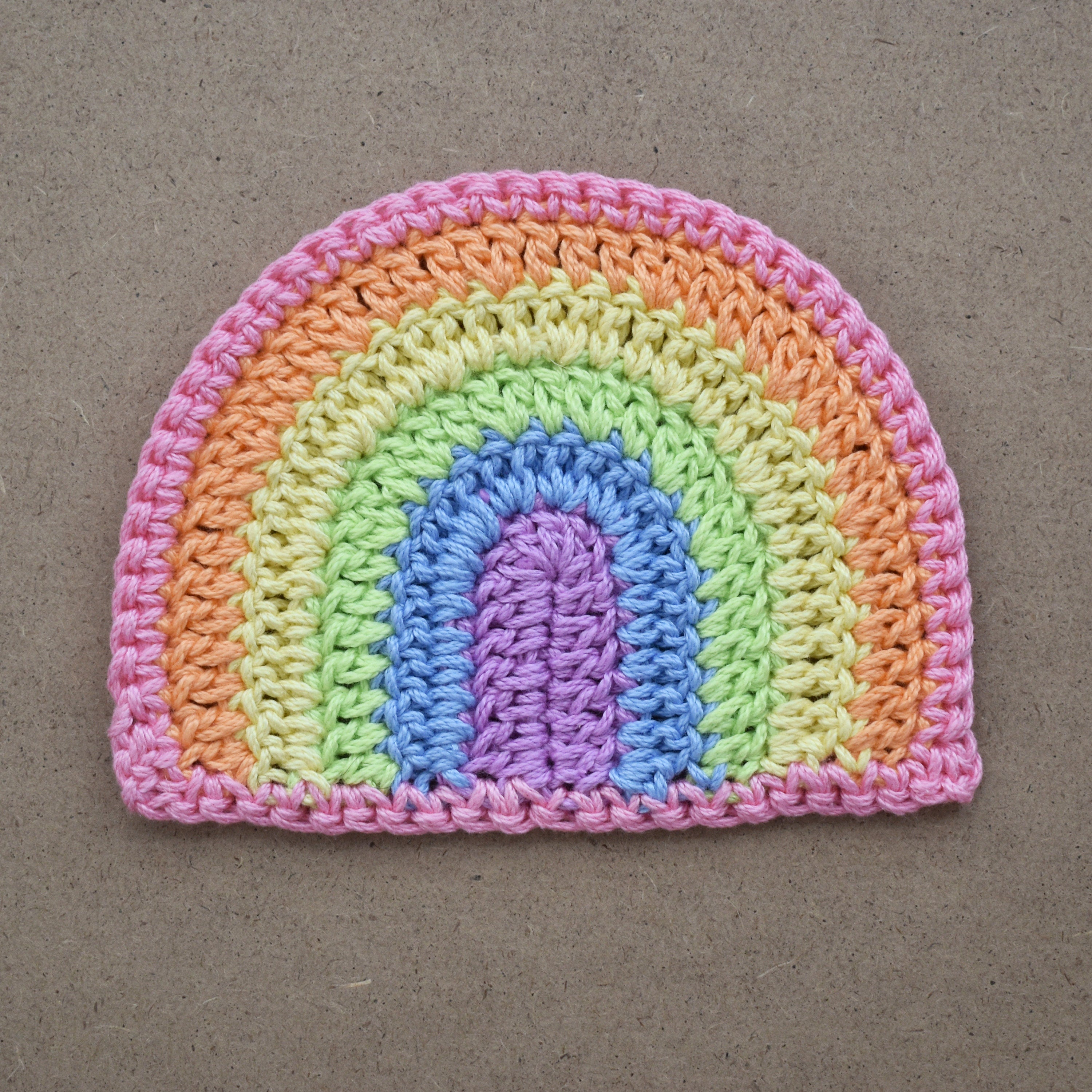 Crocheted pastel rainbow applique on a natural kraft background.