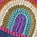 Close-up of a colorful crocheted patch with green, blue, purple, and pink colors on a denim background.