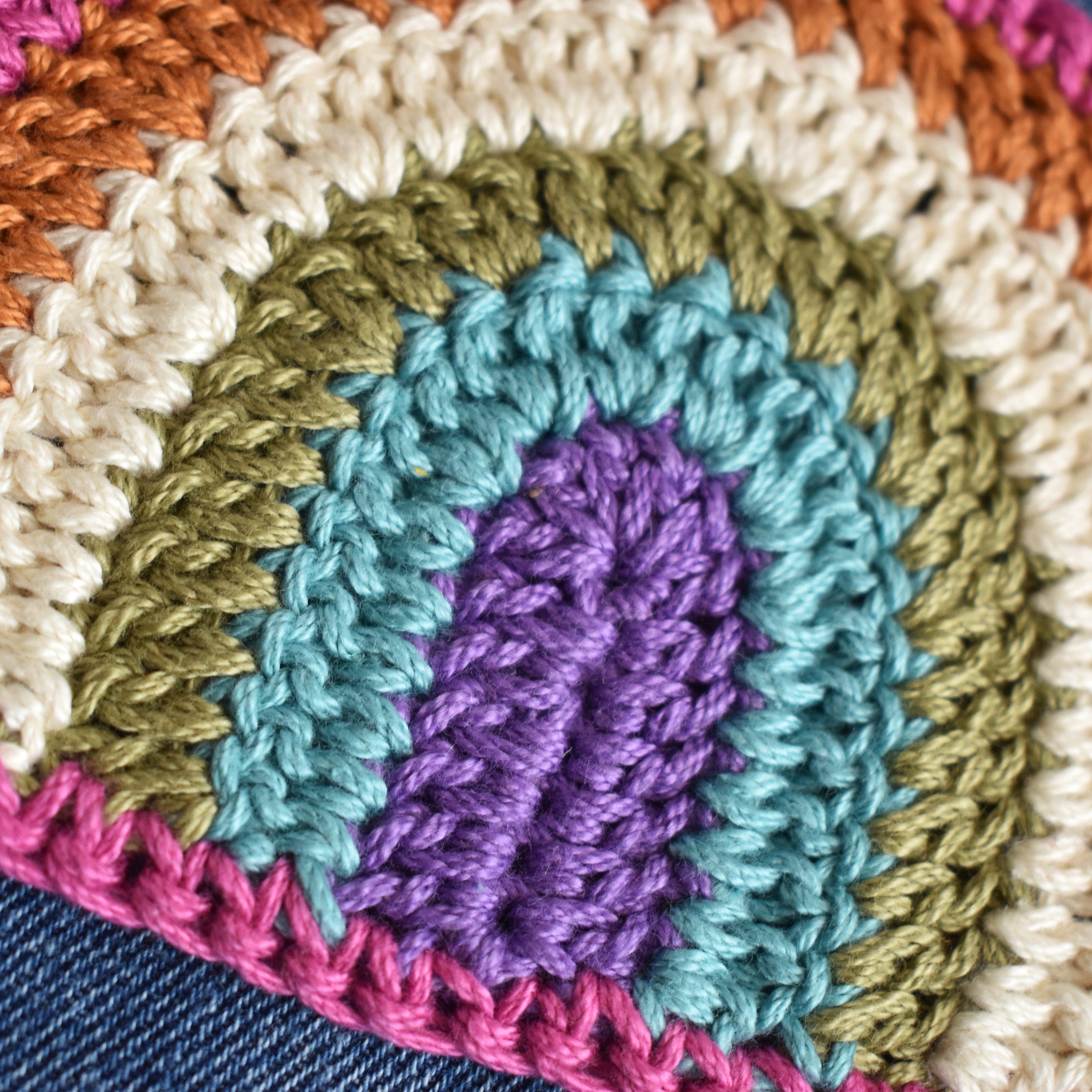Close-up of a colorful crocheted patch with green, blue, purple, and pink colors on a denim background.