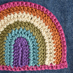 Close-up of a crocheted rainbow patch on denim fabric.