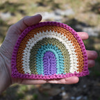 Hand holding a crocheted rainbow patch against a natural background.
