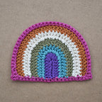 Crocheted rainbow patch on a light brown kraft textured background.