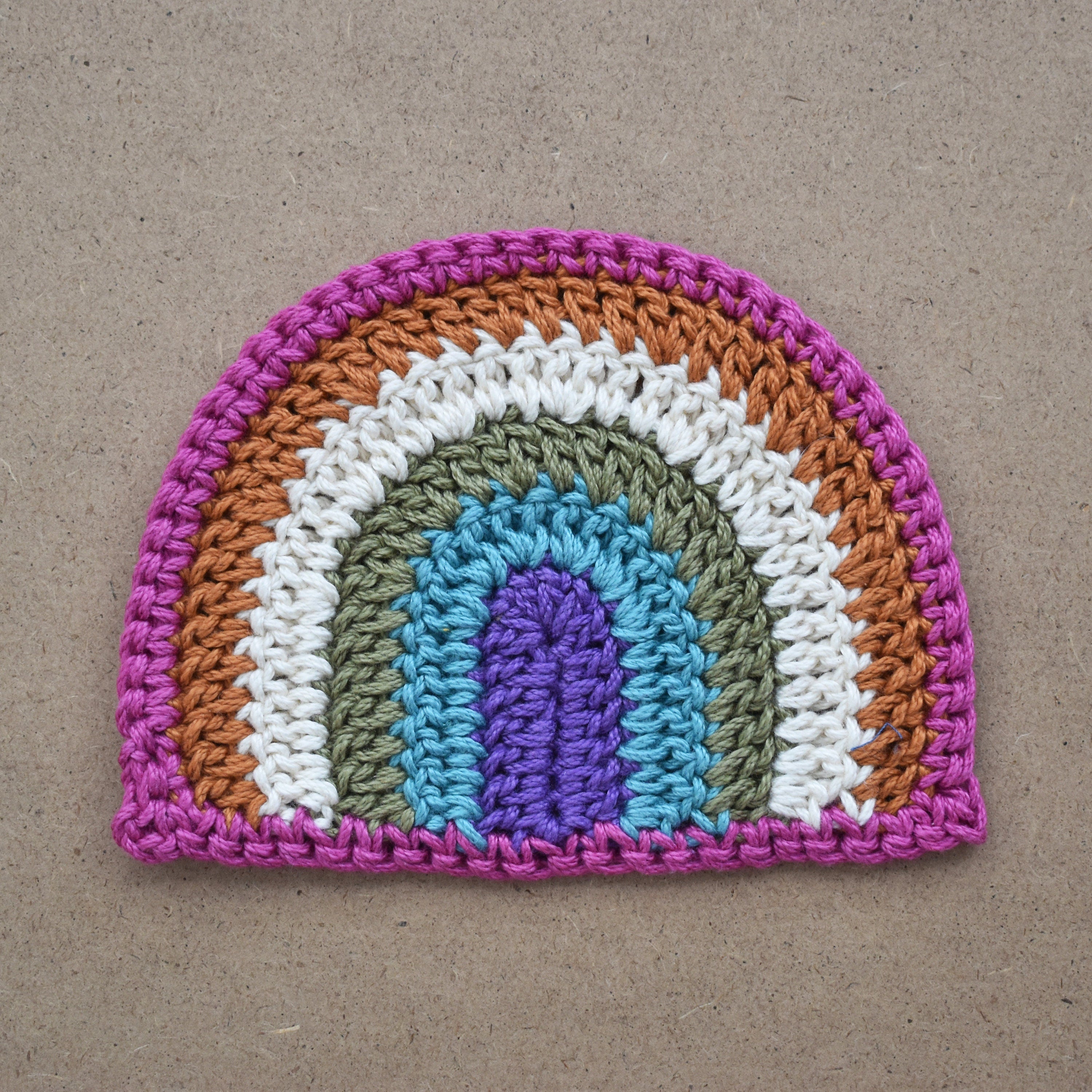 Crocheted rainbow patch on a light brown kraft textured background.