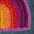 Close-up of a colorful crocheted corner with orange, red, and purple yarn on a denim background.
