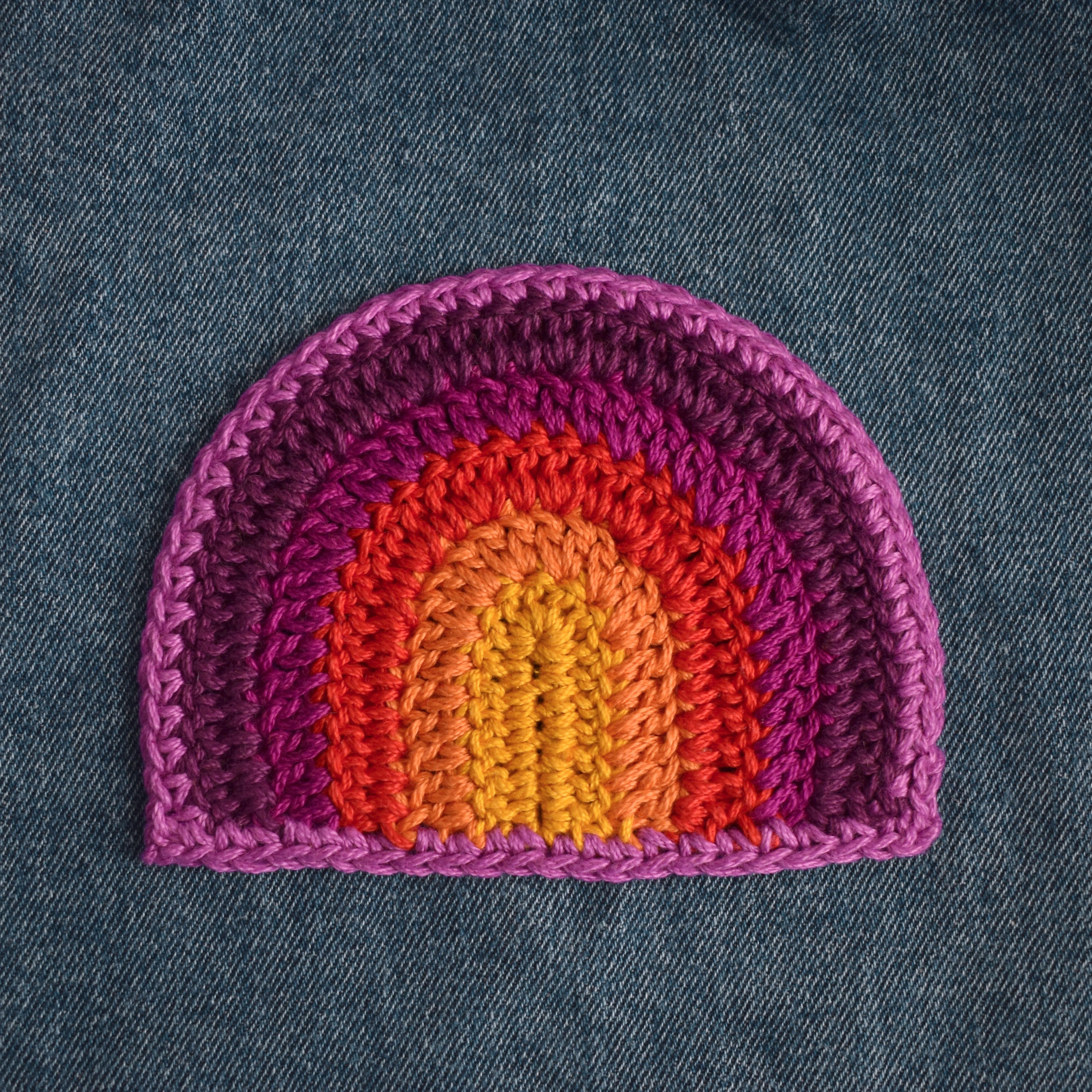 Crocheted rainbow patch on denim fabric.