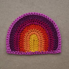 Crocheted rainbow patch on a textured brown background.