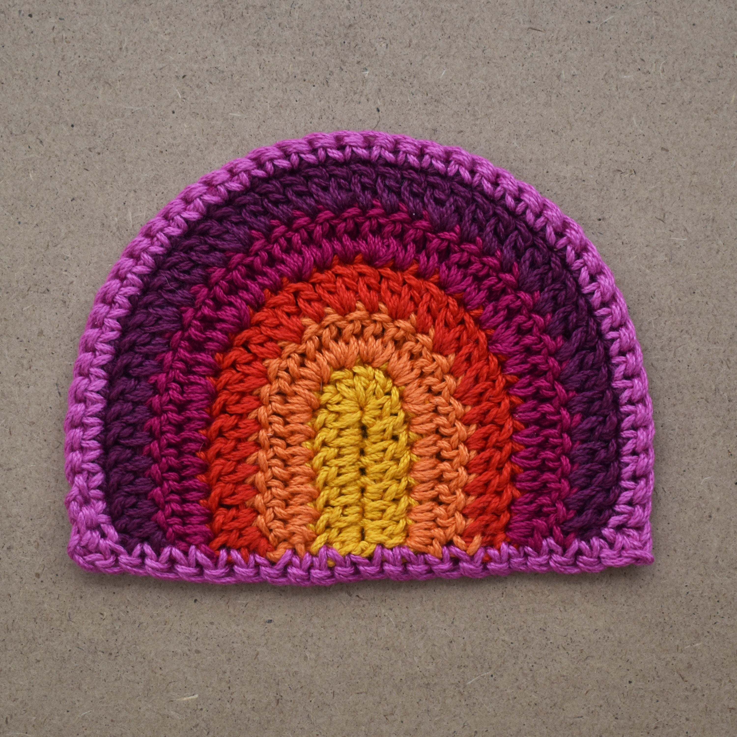 Crocheted rainbow patch on a textured brown background.