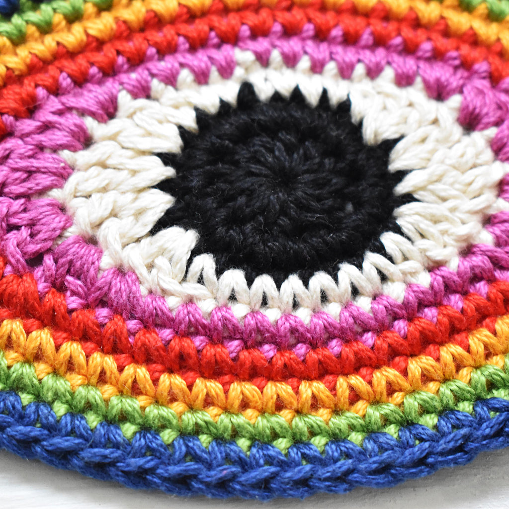 Close-up view of a crocheted eye-shaped patch in rainbow colors.