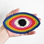 Hand holding a colorful crocheted eye-shaped applique against a white background.