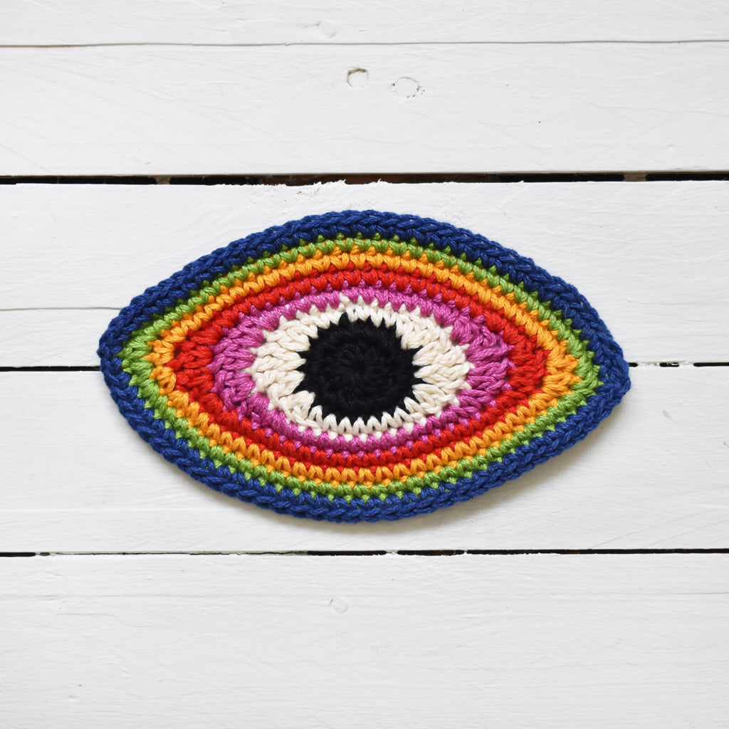 Crocheted multicolored eye-shaped patch on a white wooden surface.