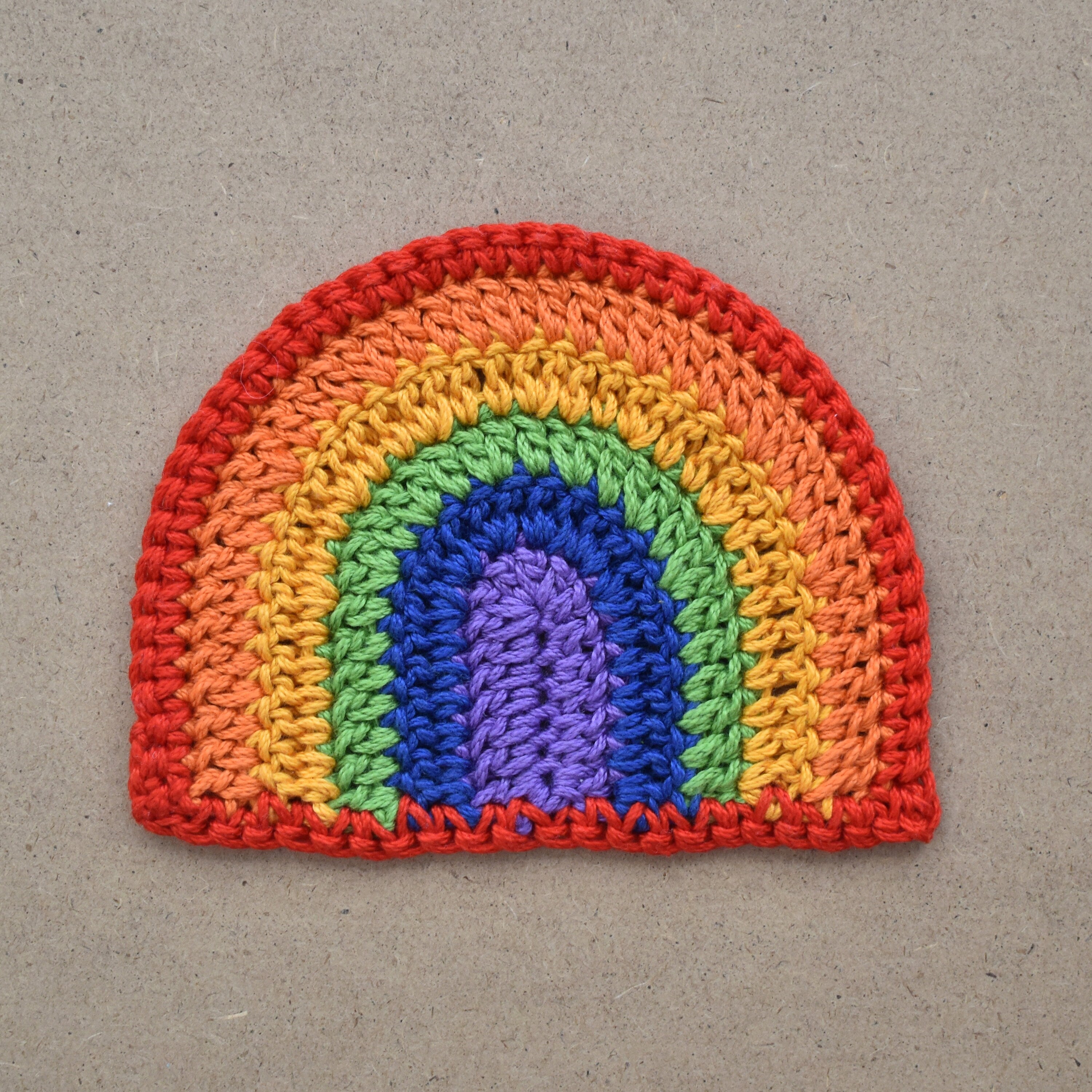 Crocheted rainbow applique on a textured kraft background.