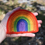 Hand holding a crocheted rainbow patch against a natural background.