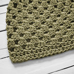 Close-up of a green knitted hat on a white wooden surface.