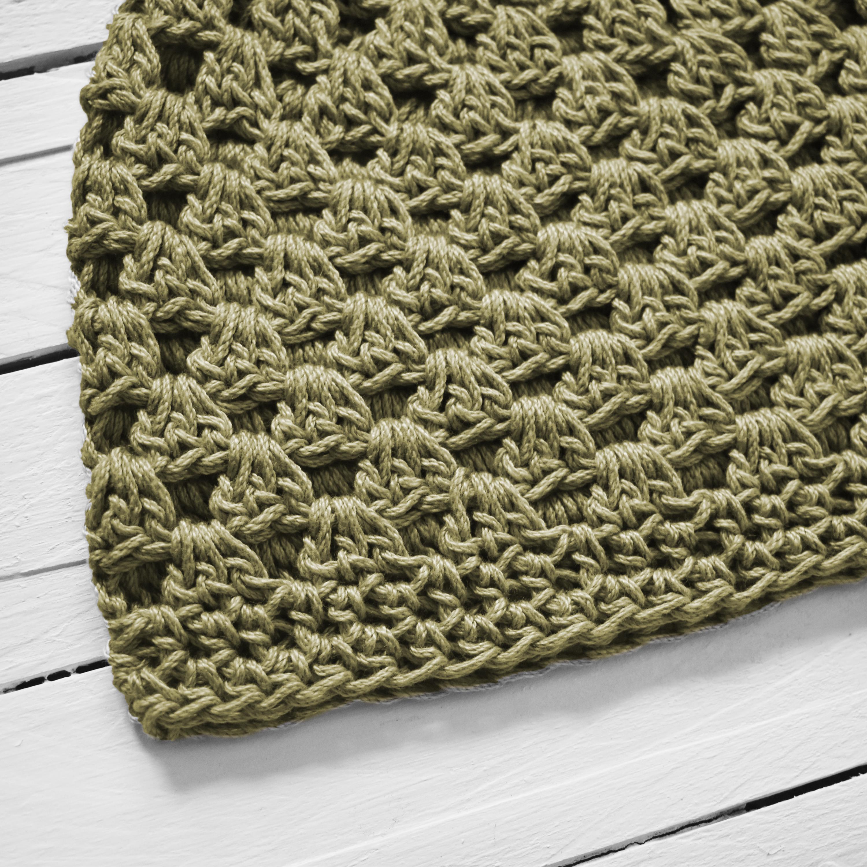 Close-up of a green knitted hat on a white wooden surface.