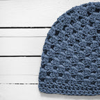 Close-up of a blue crocheted beanie on a white wooden surface.