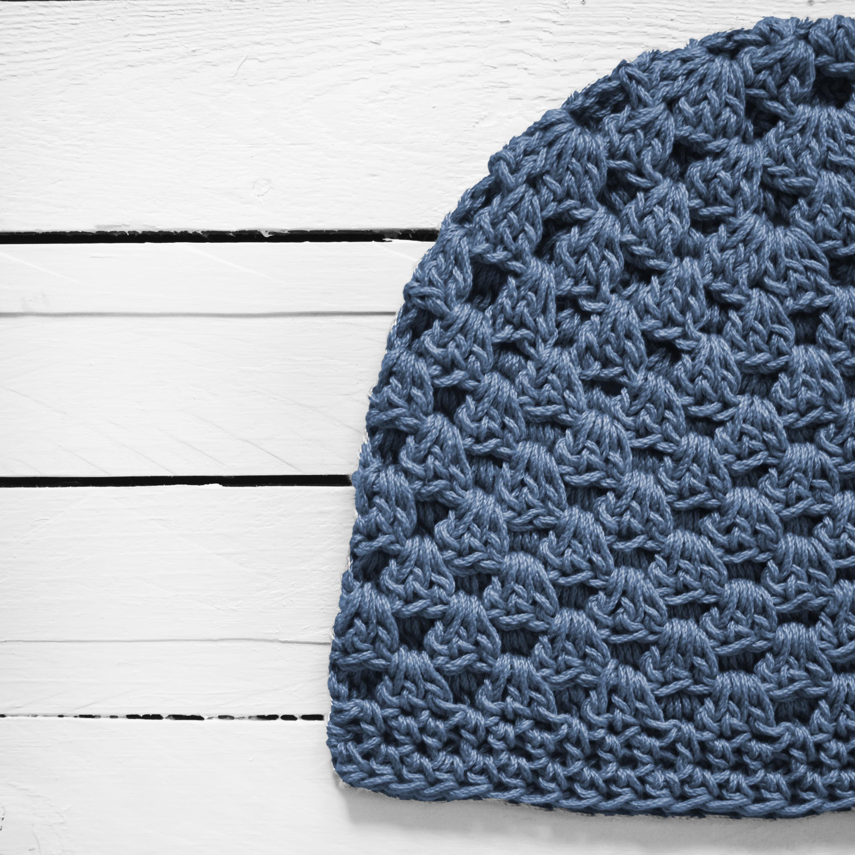 Close-up of a blue crocheted beanie on a white wooden surface.