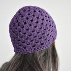 Purple knitted beanie worn by a person on a neutral background.