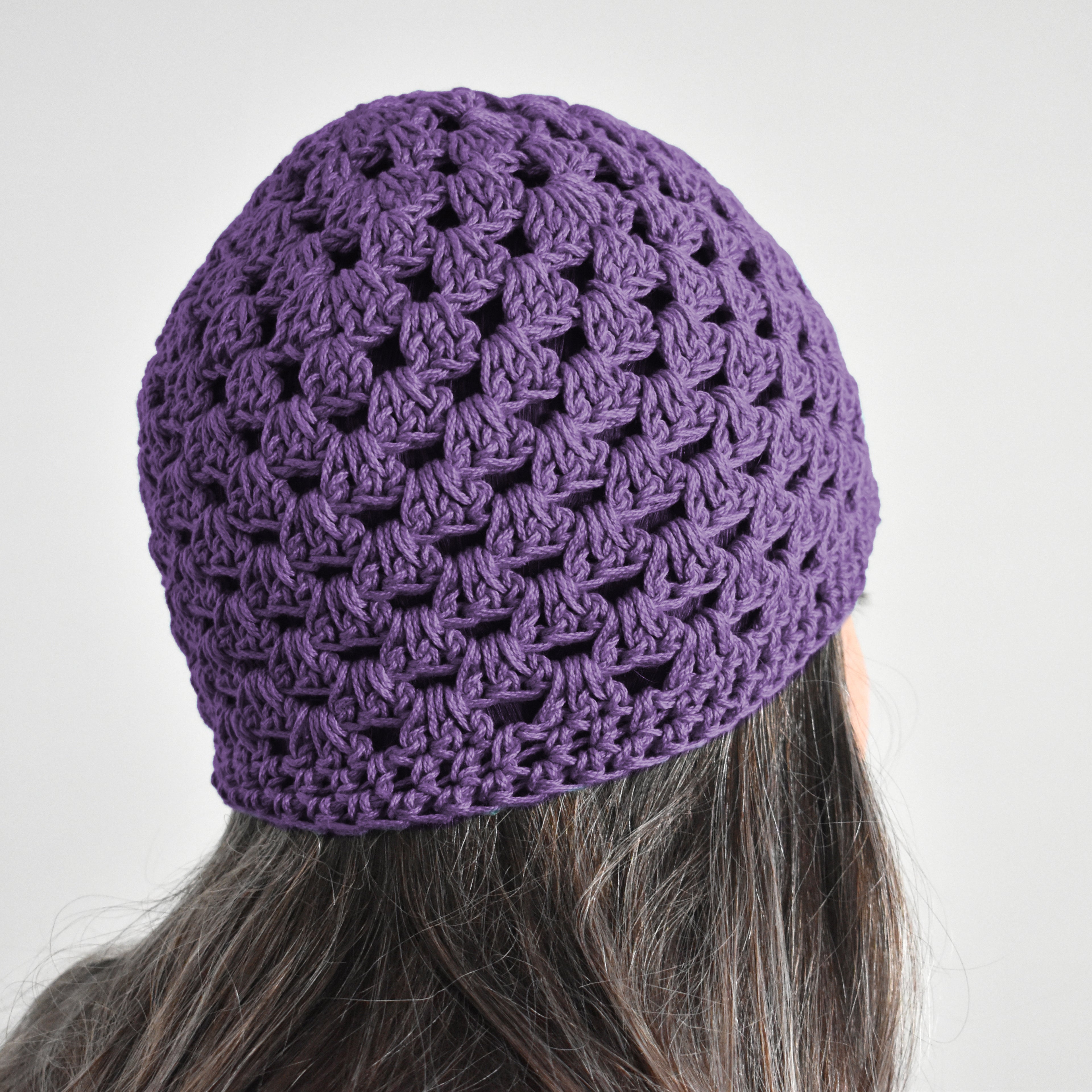 Purple knitted beanie worn by a person on a neutral background.